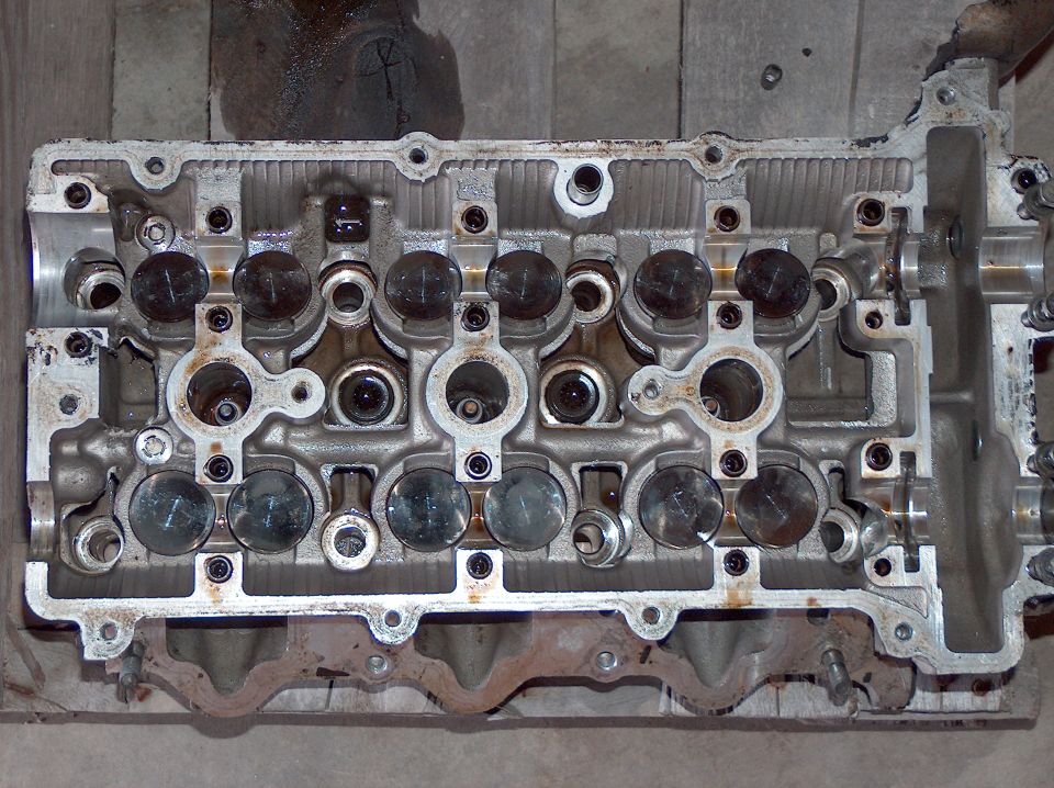 Bare DOHC cylinder head with lifters exposed, camshafts removed, sitting on wood boards