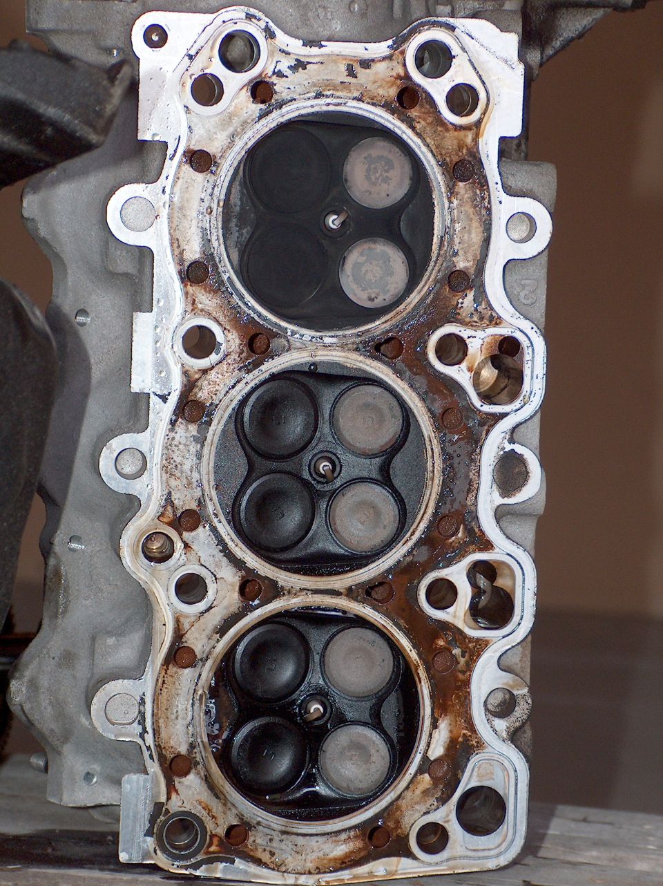 Removed V6 cylinder head showing three four-valve combustion chambers with carbon deposits
