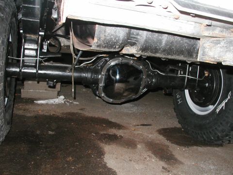 1994 Ford Bronco - Close-up view of the rear axle and suspension of a vehicle, showing the differential, brake drum, and tire with white lettering.