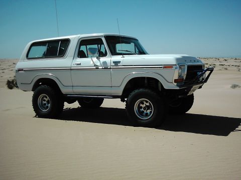 1978 Ford Bronco - A white 1978 Ford Bronco sits on a sandy terrain under a clear blue sky.