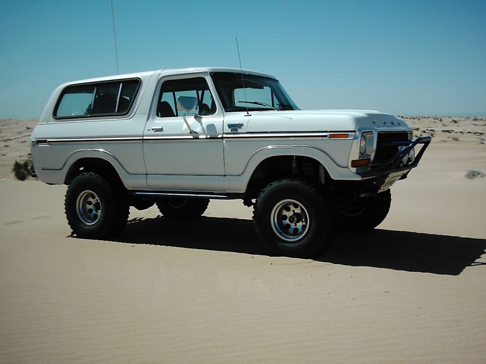 White 1978 Ford Bronco with chrome trim and off-road tires parked on sand dunes
