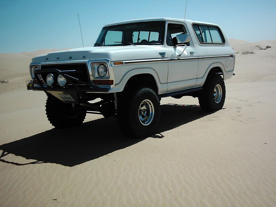White 1978 Ford Bronco with off-road bumper and lights in sand dunes