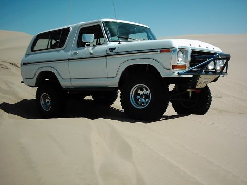 1978 Ford Bronco - A white 1978 Ford Bronco is shown on sand dunes, equipped with off-road tires and a protective brush guard.