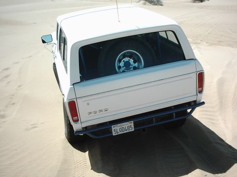 1978 Ford Bronco - White 1978 Ford Bronco parked in sand dunes with spare tire visible inside.