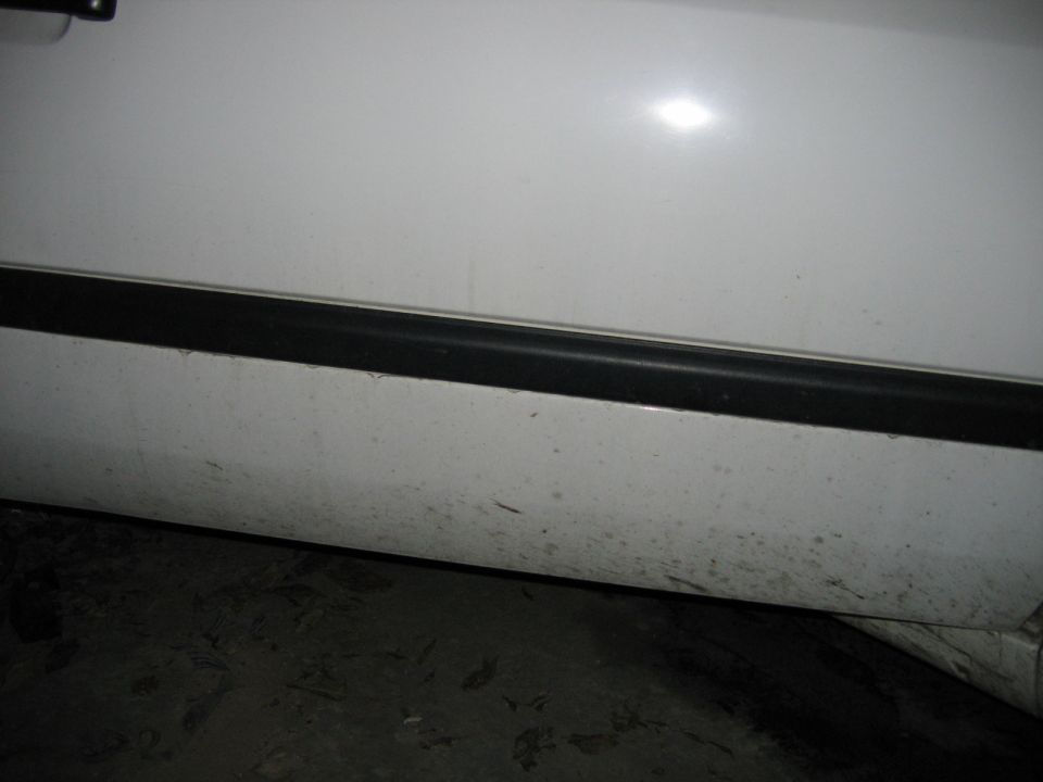 Close-up of white body panel with horizontal black rub strip, dirty concrete floor below