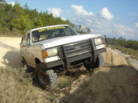 1989 Ford Bronco - This SUV is navigating a sandy incline with trees and power lines in the background.