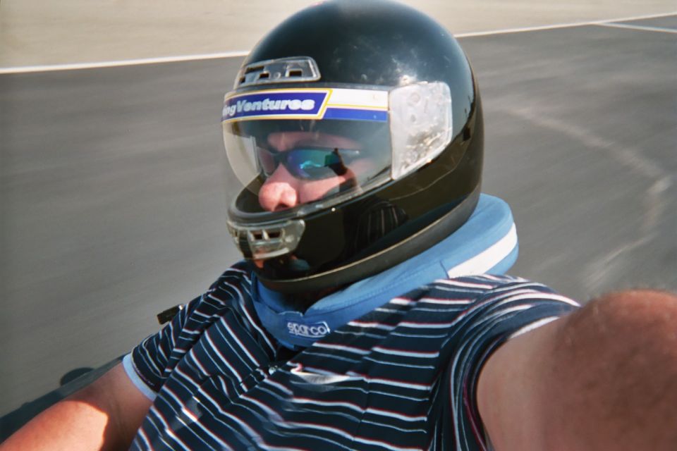 Selfie of a man in a dark racing helmet and striped shirt on a track