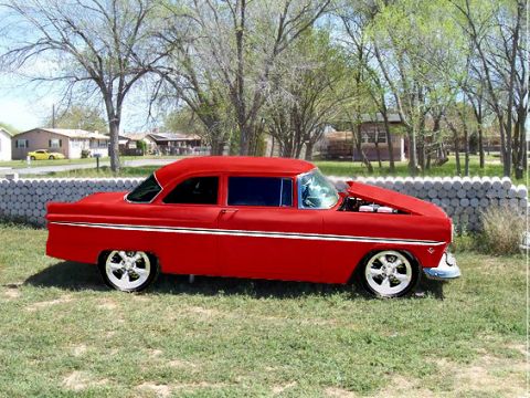 1955 Ford Customline - A bright red 1955 Ford Customline is parked on a grassy lawn with its hood raised, revealing the engine compartment.