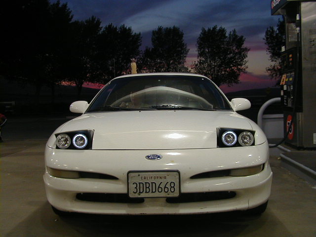 Front of white Ford Probe with halo projector headlights and California plate 3DBD668 at dusk gas station