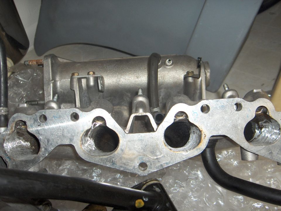 Aluminum intake manifold showing four ports and mounting flange with studs.