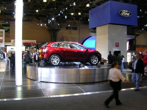 2000 Pontiac Trans Am - A red SUV is displayed on a platform at an auto show, with a large Ford sign visible.