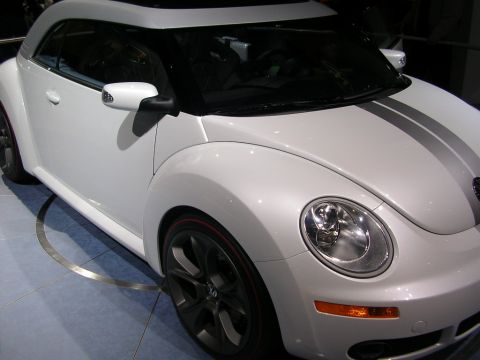 2000 Pontiac Trans Am - A white Volkswagen Beetle convertible with racing stripes is displayed at an auto show.