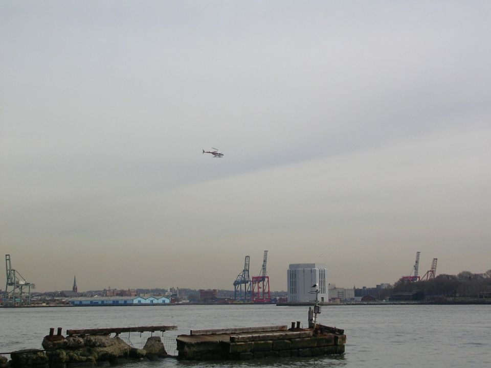 Helicopter flying over a harbor with cranes and buildings in the background