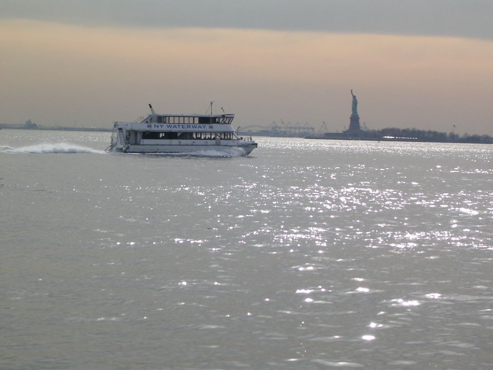 Ferry boat labeled NY WATERWAY moving on water, Statue of Liberty visible in distance