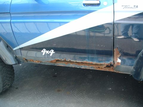1979 Ford Bronco - The lower section of a blue SUV door shows significant rust damage and a '4x4' decal.