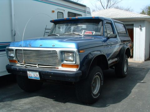 1979 Ford Bronco - This blue 1979 Ford Bronco is parked next to an RV and a garage, with a "FOR SALE" sign visible in the windshield.