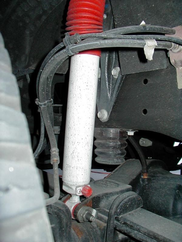 White shock absorber with red boot on front suspension underbody with coil spring and brake lines.