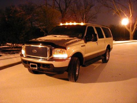 2002 Ford Excursion - A tan Ford Excursion is parked in the snow at night, illuminated by its headlights and roof lights.