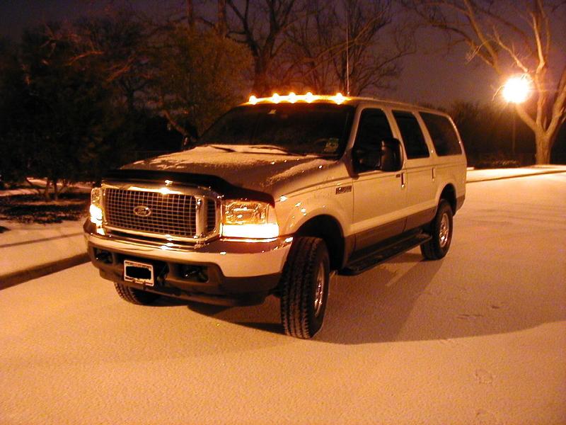 Tan Ford Excursion SUV at night on snowy lot, headlights and roof clearance lights on