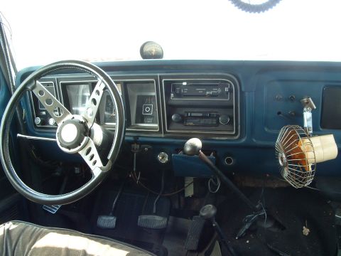 1979 Ford Bronco - The dashboard of an older truck shows the steering wheel, radio, and a fan attached to the dash.