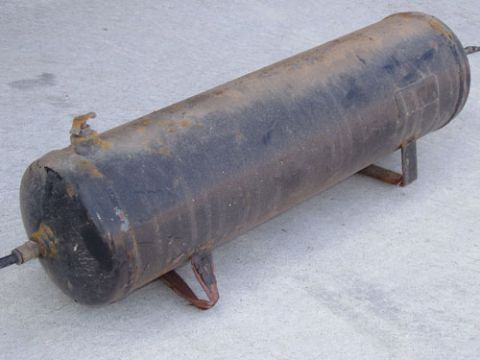 1995 Ford Bronco - A cylindrical steel air tank with welded mounting feet lies on a concrete slab, its black paint faded and streaked with surface rust. Threa…