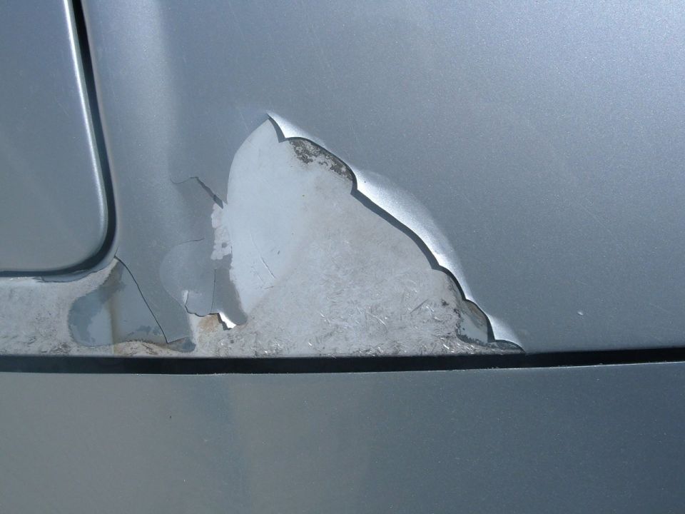 Close-up of silver body panel corner with cracked peeling clearcoat exposing primer underneath