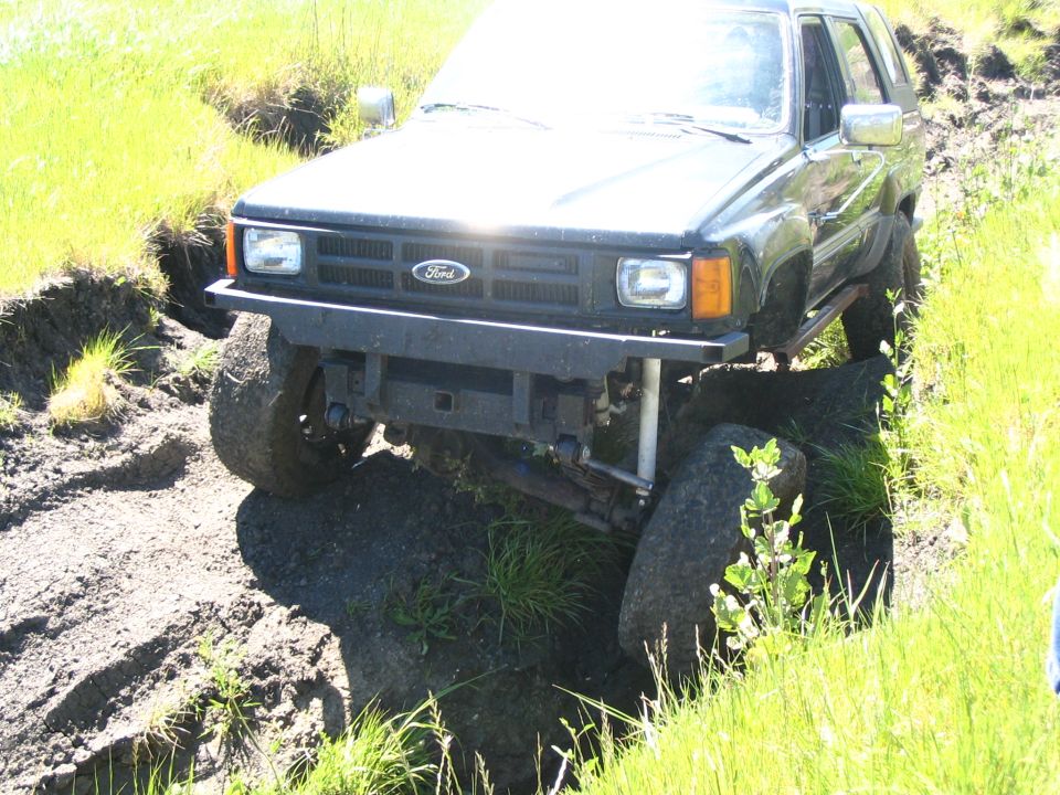 Front of black Ford pickup with lift, leaf springs and shocks exposed, perched on dirt embankment