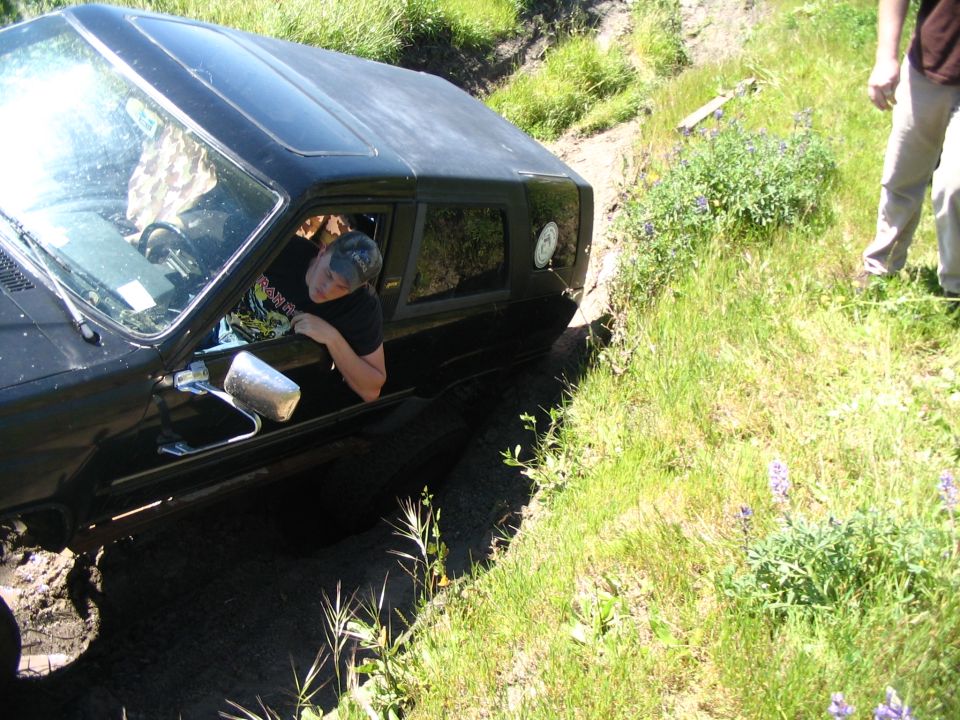 Black SUV tipped in a ditch with driver in cap leaning out the window, mirror dangling