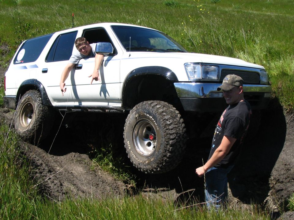 White lifted Toyota 4Runner on mud trail, man leaning out window, second man standing in rut