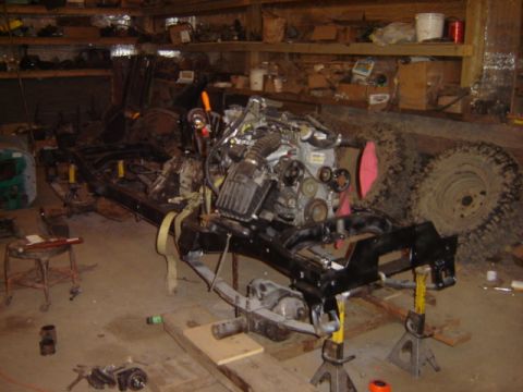 1992 Ford Bronco - The chassis and engine of a vehicle are disassembled and supported by jack stands in a cluttered garage.