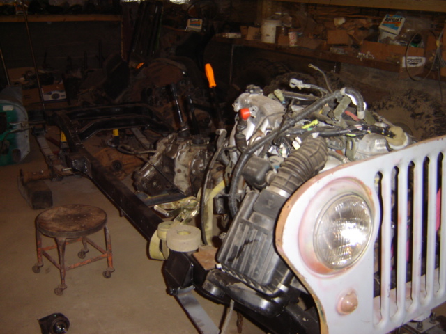 Vehicle chassis and engine assembly in a workshop, with a stool nearby