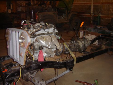 1992 Ford Bronco - An engine and transmission are mounted to a chassis frame, with a Jeep-like front grille visible in the foreground.
