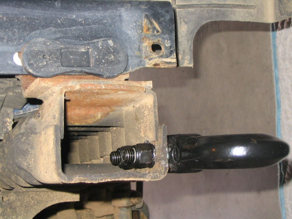 Underbody view of a suspension component and a black-handled tool wedged against a frame rail