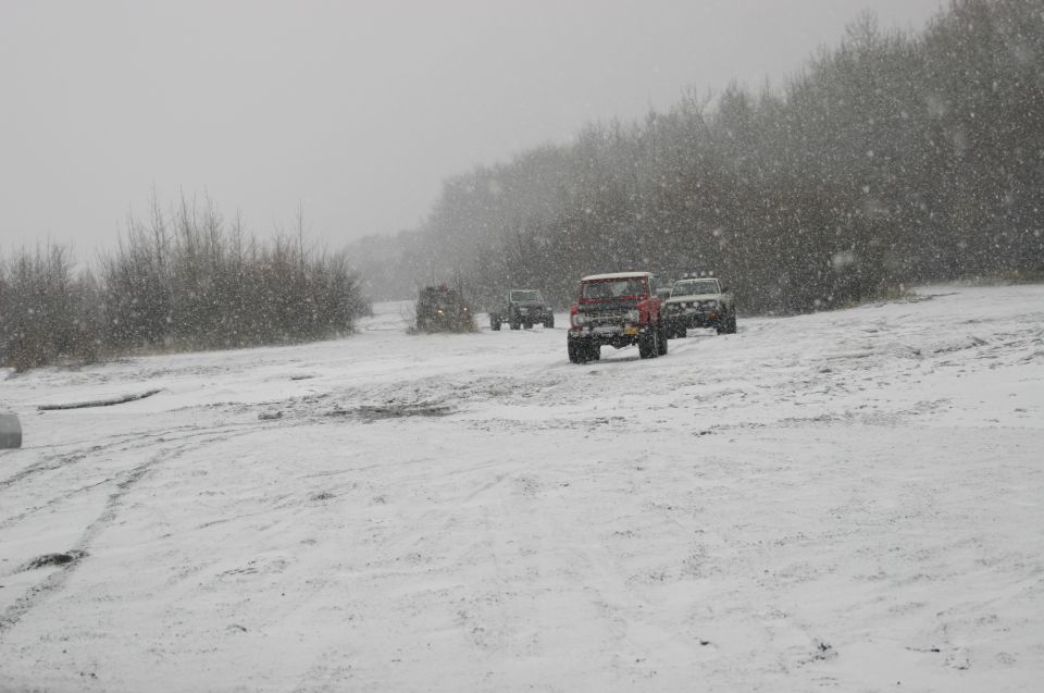 Several off-road vehicles driving on a snowy path with trees in the background