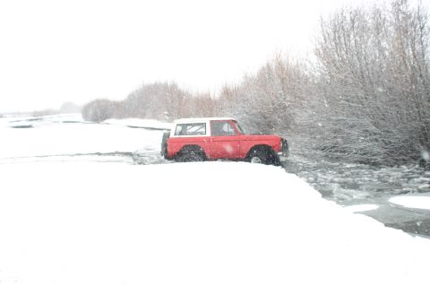 2003 Jeep TJ - A red and white SUV is partially submerged in icy water during a snowstorm.
