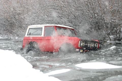 2003 Jeep TJ - Classic red Ford Bronco navigates through icy water during a winter off-road excursion.