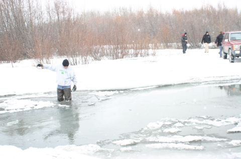 2003 Jeep TJ - A person wades through icy water while others stand by a red SUV on a snowy bank.