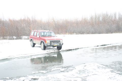 2003 Jeep TJ - A red Jeep Cherokee XJ is parked on the snowy bank next to a partially frozen body of water.