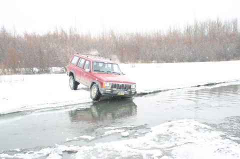 2003 Jeep TJ - Red Jeep Cherokee XJ navigates icy water in a snowy landscape.