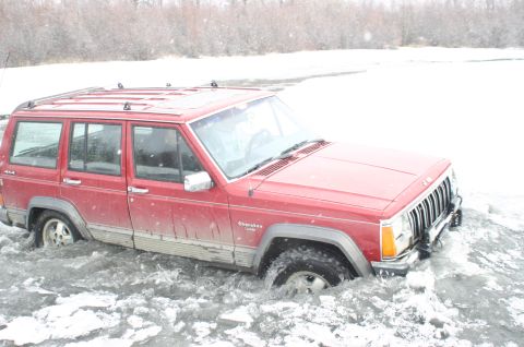 2003 Jeep TJ - A red Jeep Cherokee XJ is partially submerged in icy water, with snow falling.