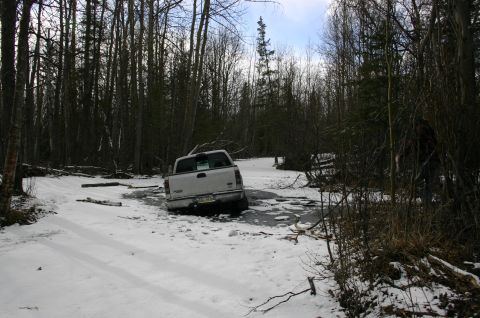 2003 Jeep TJ - A white pickup truck is stuck in a snowy, icy clearing surrounded by trees.