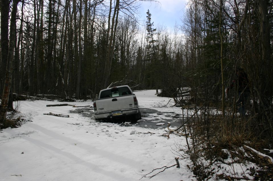 White pickup truck stuck in icy snow in a wooded area