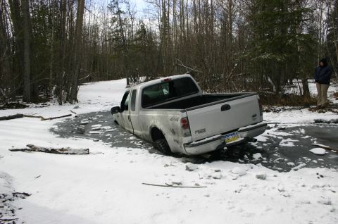 2003 Jeep TJ - Pickup truck is stuck in ice and snow, with a person standing in the background.