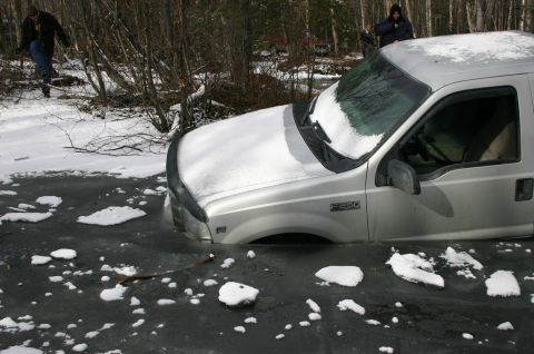 2003 Jeep TJ - A silver Ford F-250 is partially submerged in ice and snow, with two individuals observing the scene.