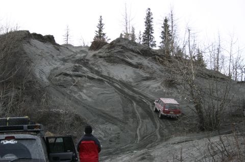 2003 Jeep TJ - A red SUV navigates a challenging dirt incline, while another vehicle waits below.