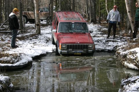 2003 Jeep TJ - Jeep Cherokee XJ navigates an icy stream in a wooded area with onlookers present.