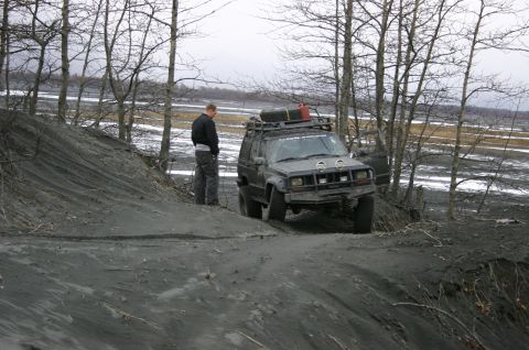 2003 Jeep TJ - A modified Jeep Cherokee XJ navigates a muddy incline in a barren landscape.