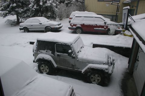 2003 Jeep TJ - A silver Jeep Wrangler is parked in a snow-covered driveway alongside other vehicles.