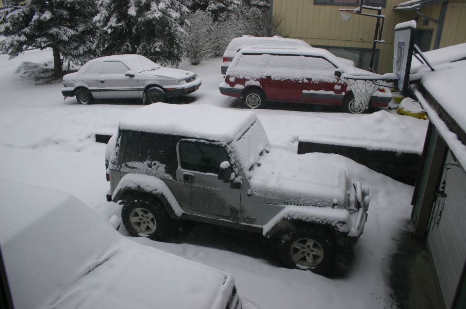 Silver Jeep Wrangler covered in snow, parked in a driveway