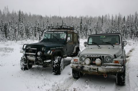 2003 Jeep TJ - Two Jeeps, likely 2003 models, sit in a snow-covered landscape with a dense forest in the background.